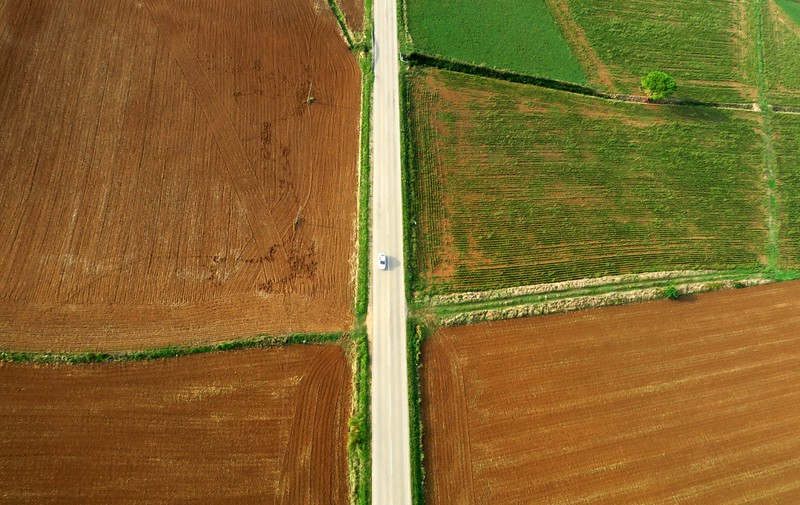An overhead perspective shot of a car driving in a rural area 